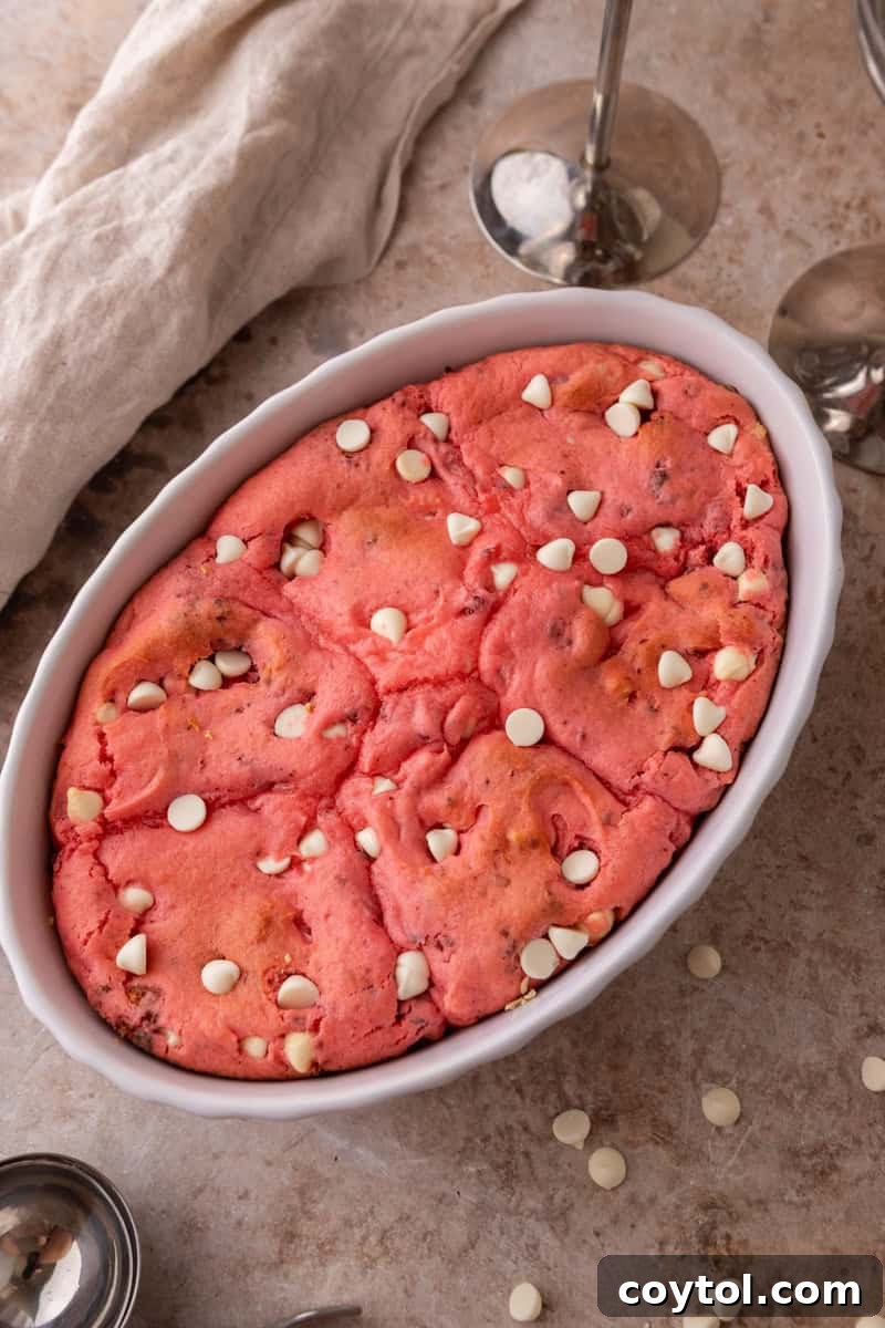 Freshly baked strawberry scoopable cookies in a white oval baking dish with white chocolate chips on top