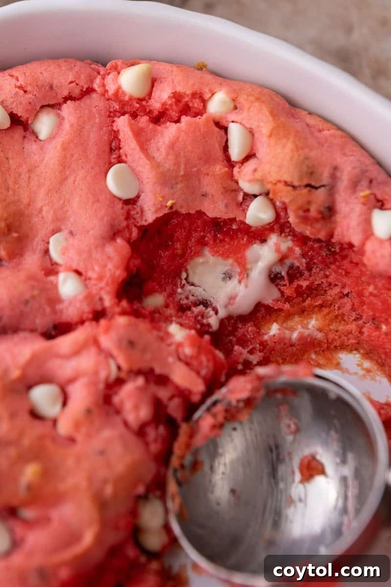 Strawberry scoopable cookies being scooped from a baking dish revealing a soft gooey center