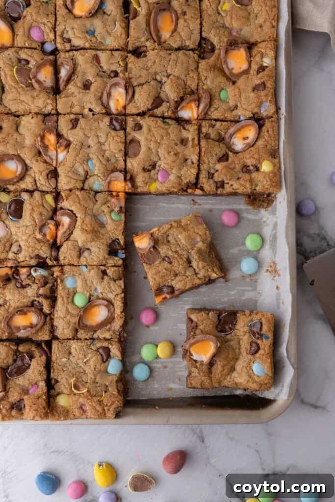 Effortless Easter Treats: Over 20 Recipes for a Memorable Spring Feast 11 Cadbury egg cookie bars sliced into squares in a parchment lined baking pan with pastel M&Ms and Cadbury creme eggs baked in