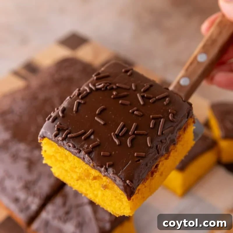 Vibrant Brazilian Carrot Cake with Decadent Chocolate Glaze 2 A slice of bright orange Brazilian carrot cake with thick chocolate glaze and chocolate sprinkles being lifted with a wooden-handled knife, showcasing its moist texture.