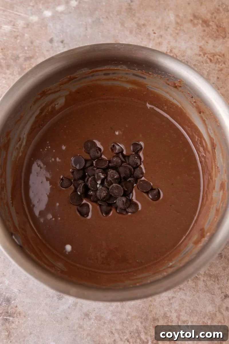 Vibrant Brazilian Carrot Cake with Decadent Chocolate Glaze 11 Dark chocolate chips being added to the warm, glossy chocolate glaze in a saucepan, ready to be stirred in for the final touch.