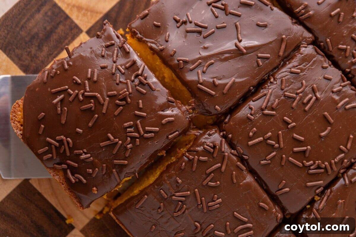 Vibrant Brazilian Carrot Cake with Decadent Chocolate Glaze 3 Overhead view of a perfectly sliced Brazilian carrot cake on a checkered wood cutting board, with a spatula lifting one piece to reveal its tender crumb and rich chocolate glaze.