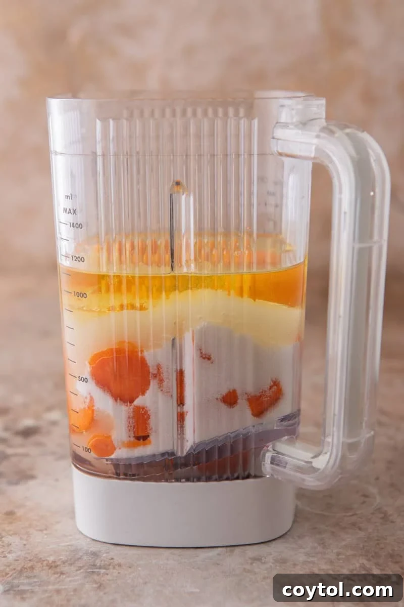 Vibrant Brazilian Carrot Cake with Decadent Chocolate Glaze 6 A blender filled with distinct layers of chopped carrots, sugar, oil, and eggs, showcasing the initial setup before blending for the Brazilian carrot cake.