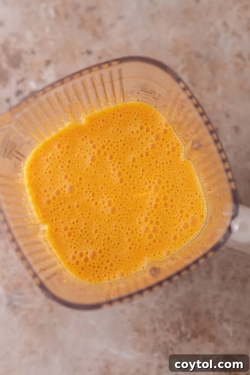 Vibrant Brazilian Carrot Cake with Decadent Chocolate Glaze 7 An overhead view of bright orange, smoothly blended cake batter inside a blender jar, featuring small air bubbles on its frothy surface, indicating readiness.