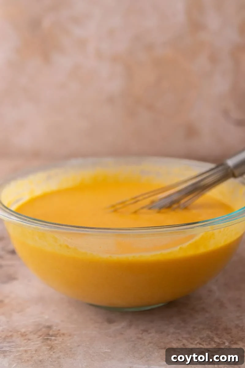 Vibrant Brazilian Carrot Cake with Decadent Chocolate Glaze 8 Smooth, vibrant orange cake batter resting in a clear glass mixing bowl, with a whisk gently positioned inside, ready for the next step.