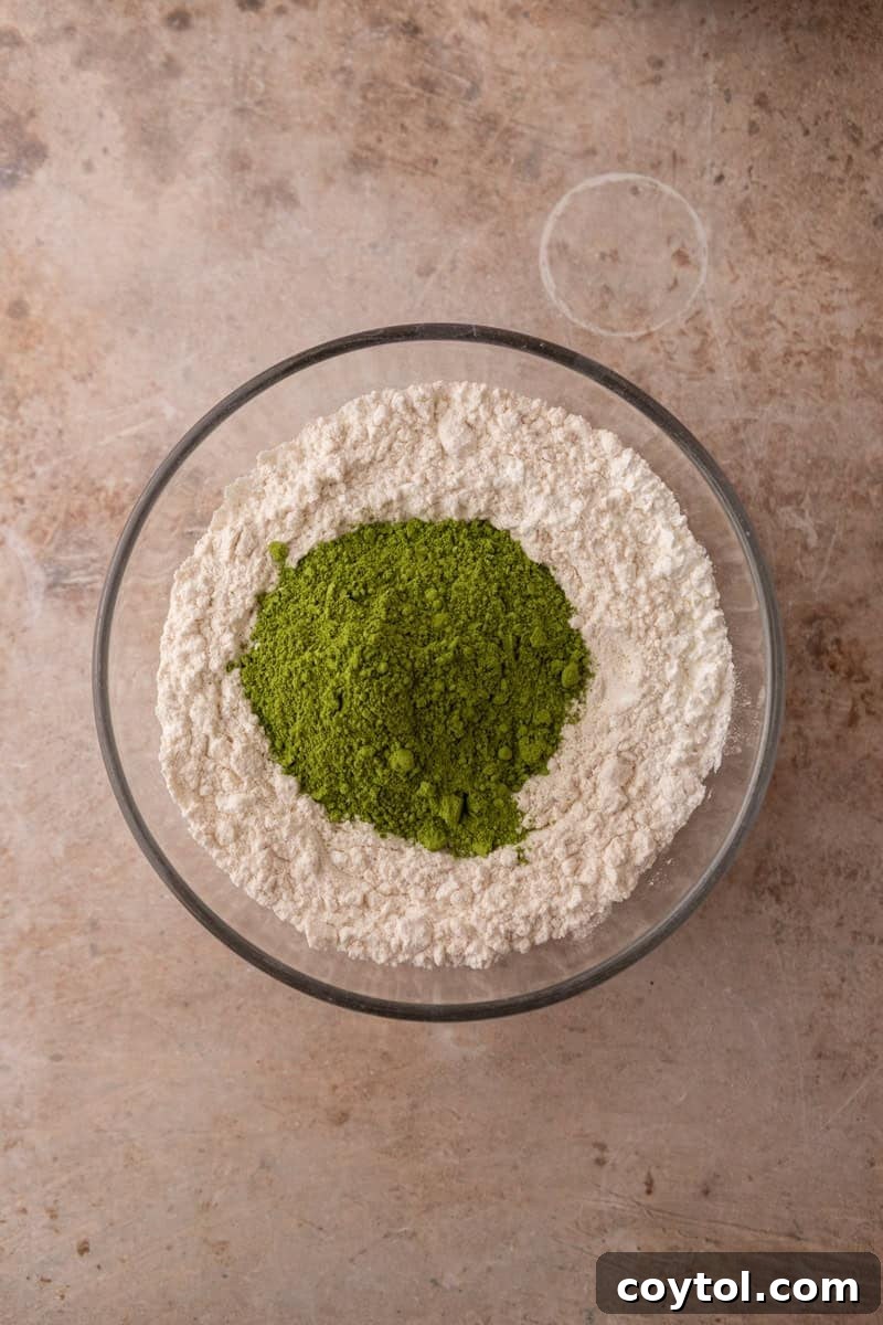 Vibrant green matcha powder on top of flour in a glass bowl before whisking the dry ingredients together