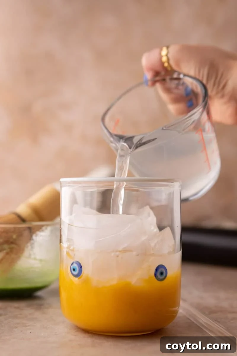 Fresh Mango Matcha Coconut Water Delight 8 pouring coconut water over ice into a glass containing mango puree for a layered drink