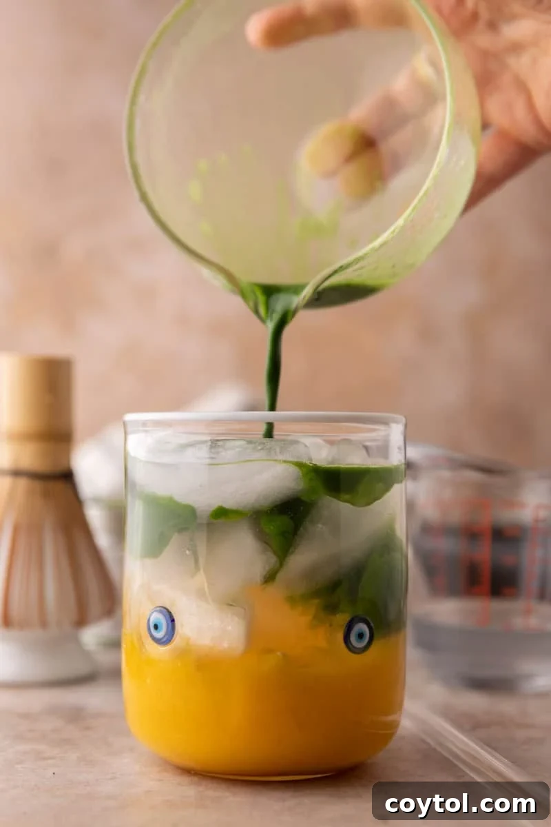 Fresh Mango Matcha Coconut Water Delight 9 slowly pouring whisked matcha over ice into the mango coconut water drink, forming a beautiful marble effect