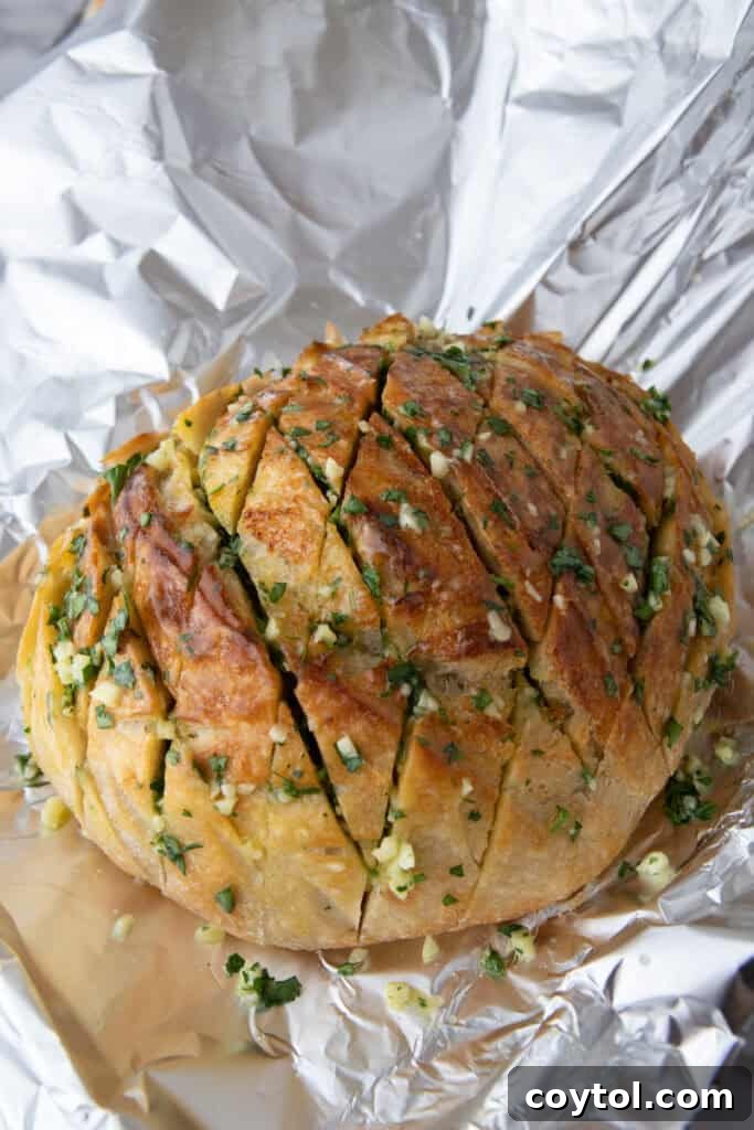 Golden Gooey Garlic Bread Pull Apart Perfection 7 Sourdough loaf generously stuffed with fragrant garlic butter and a mix of cheeses, then lightly wrapped in foil, sitting on a baking sheet and ready for its first stage of baking.