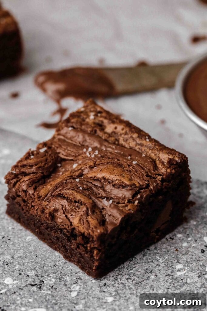 A delectable small batch Nutella brownie square, beautifully swirled with Nutella on top and revealing a fudgy chocolate interior, elegantly sprinkled with flaky sea salt, made in a loaf pan.