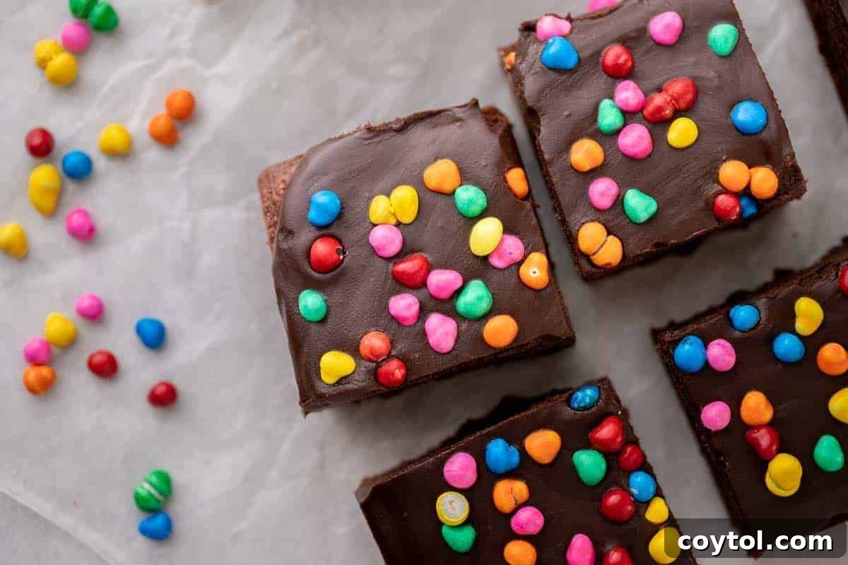 Homemade cosmic brownies, lavishly topped with a thick chocolate ganache and vibrant colorful rainbow candy chips, presented on parchment paper, scaled for a small batch.