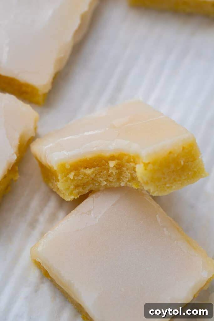 Vibrant lemon blondies, elegantly topped with a smooth lemon glaze, sliced into perfect squares, with a bite taken out of one piece to reveal the bright yellow, fudgy interior, perfect for spring.