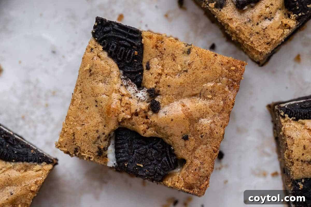 Delicious brown butter Oreo blondies, meticulously sliced into squares, revealing generous chunks of Double Stuf Oreo cookies baked directly into the chewy, golden blondie bars, an insane combination.