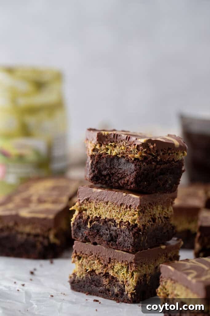 A decadent stack of three Dubai chocolate brownies, showcasing the impressive pistachio kunafa layer nestled between a fudgy brownie base and a thick, glossy chocolate ganache topping, delivering on the hype.