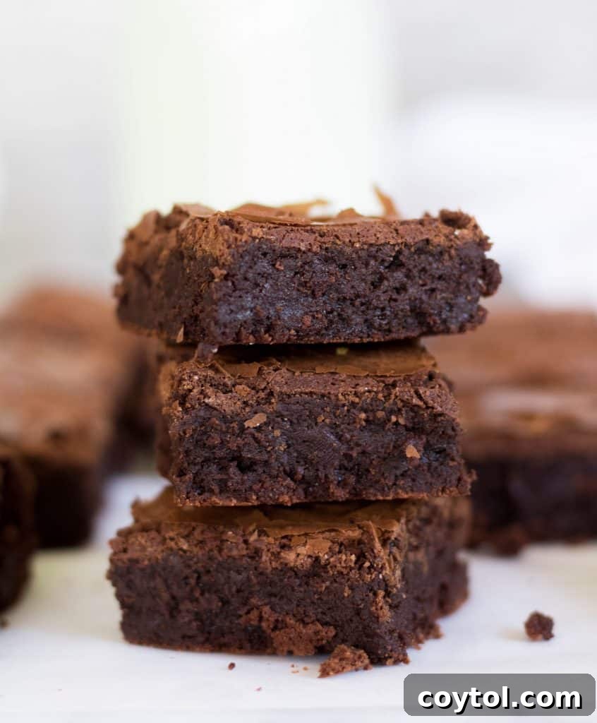 Stack of three bakery style brownies without cocoa powder, revealing their ultra-fudgy, dense interior and thin, crinkly crust on top, a true viral sensation.