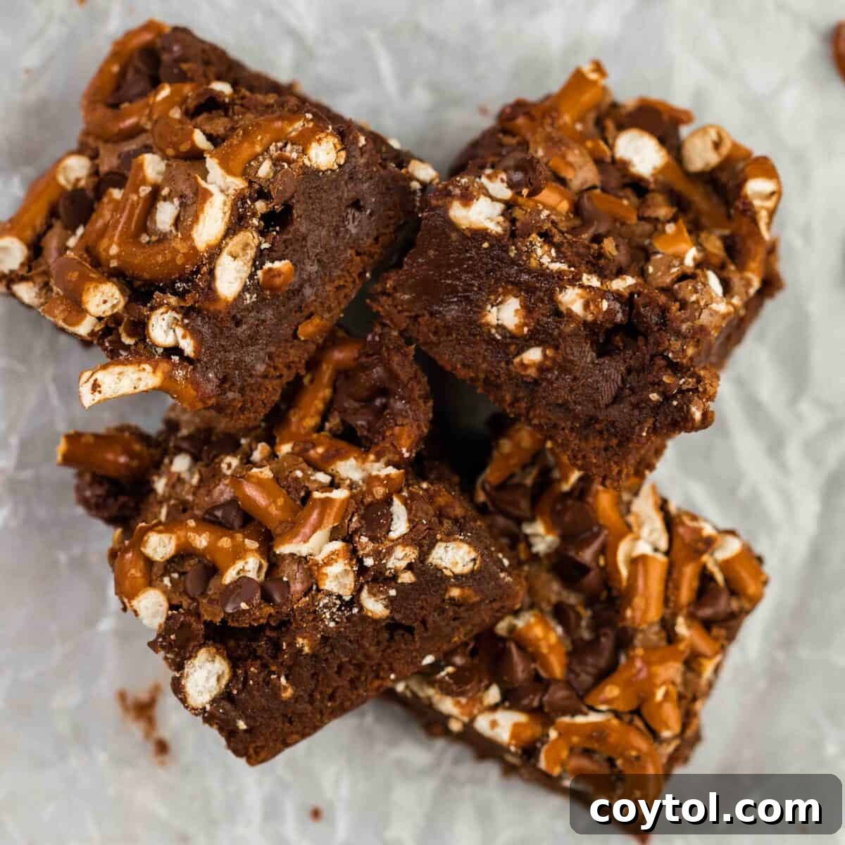 Pretzel brownies piled together, showcasing crushed pretzels and luscious chocolate chips beautifully baked into the fudgy chocolate brownie base on parchment paper, perfect for sweet-salty lovers.