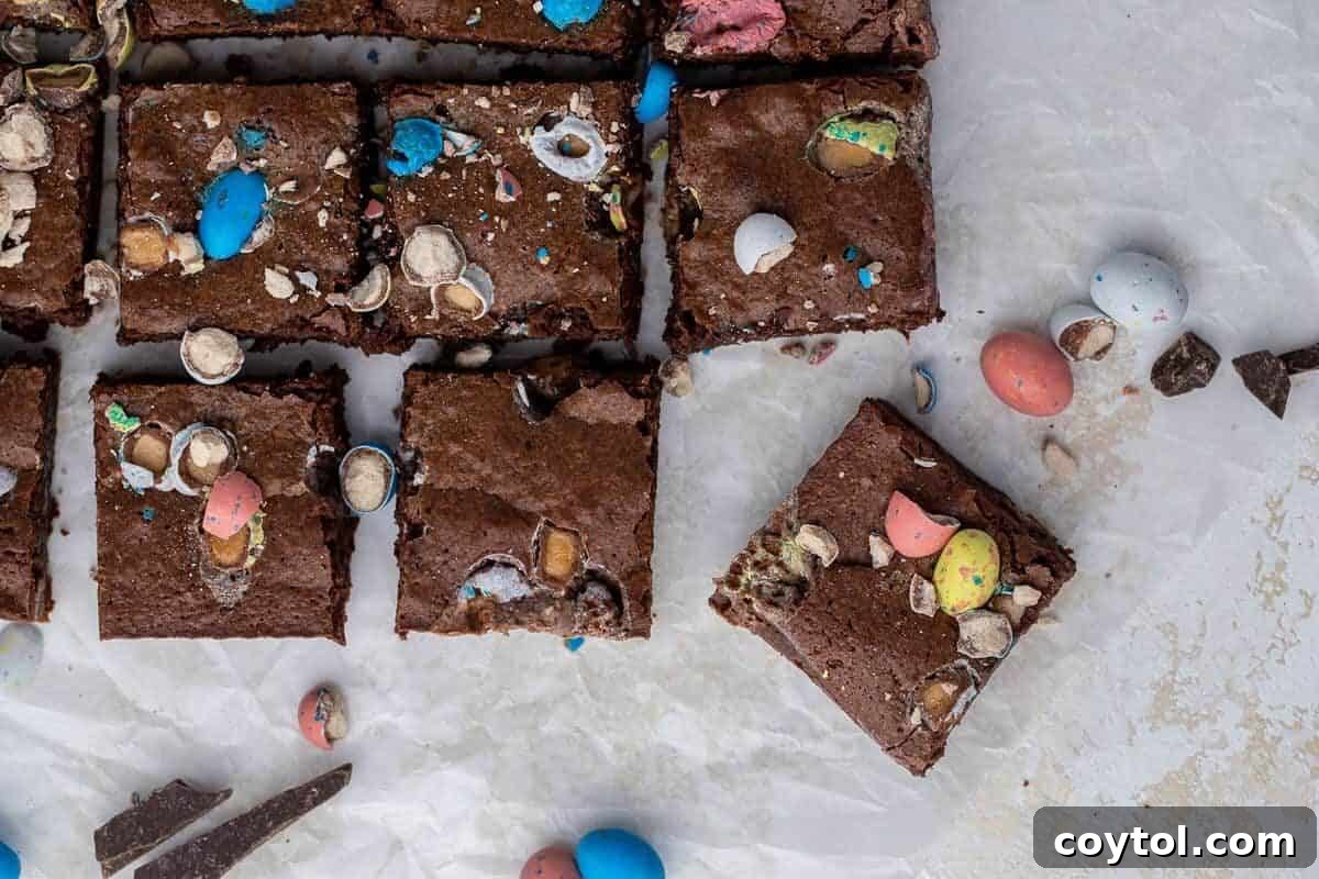 Overhead view of fudgy Easter mini egg brownies, neatly sliced into squares on parchment paper, lavishly topped with crushed colorful Cadbury Mini Eggs and Robin Eggs, a huge hit for spring.