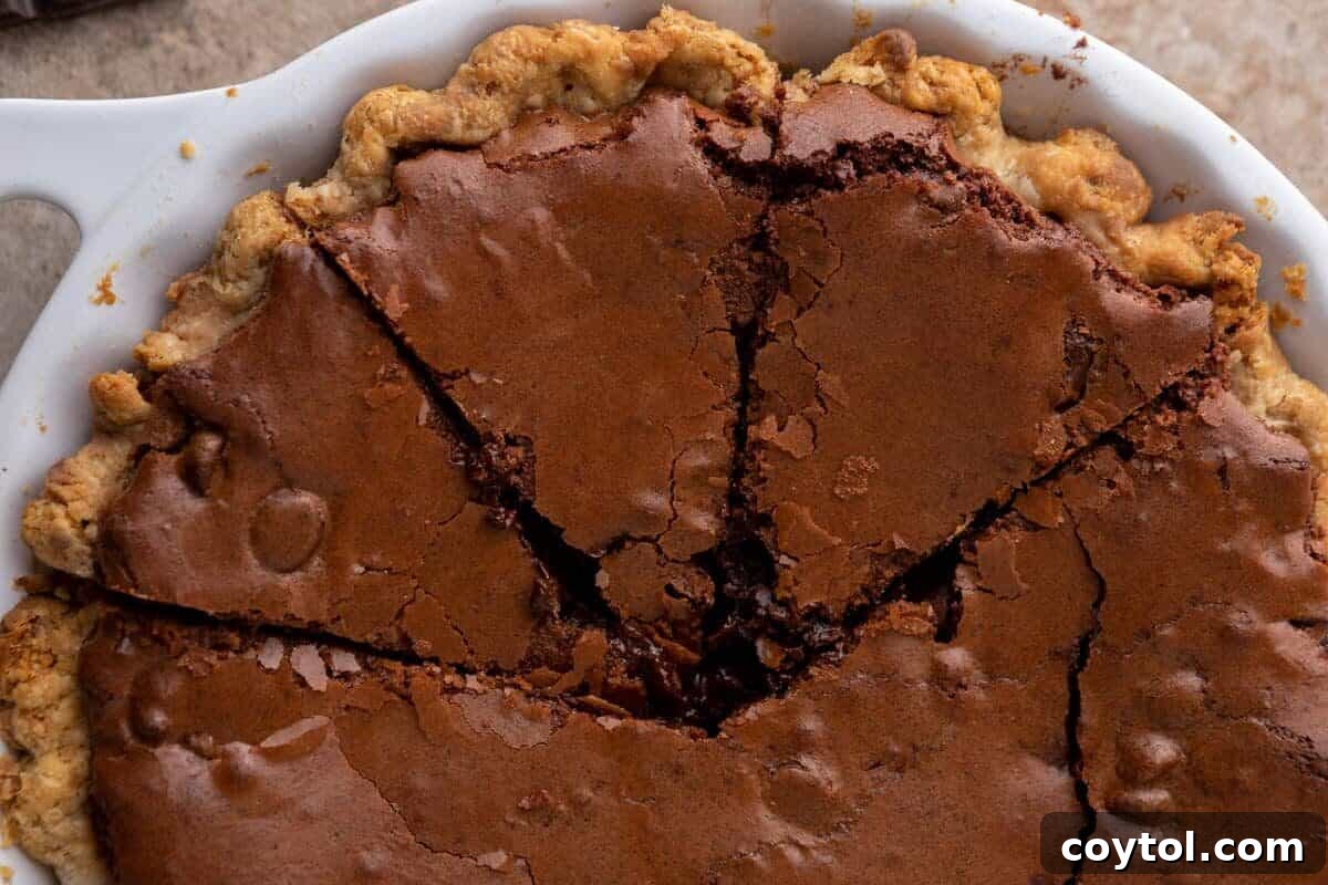 Overhead view of a luscious brownie pie, beautifully baked in a white pie dish with a golden, flaky pie crust and a rich, fudgy chocolate brownie filling, neatly sliced into triangular pieces, ultimate dessert experience.