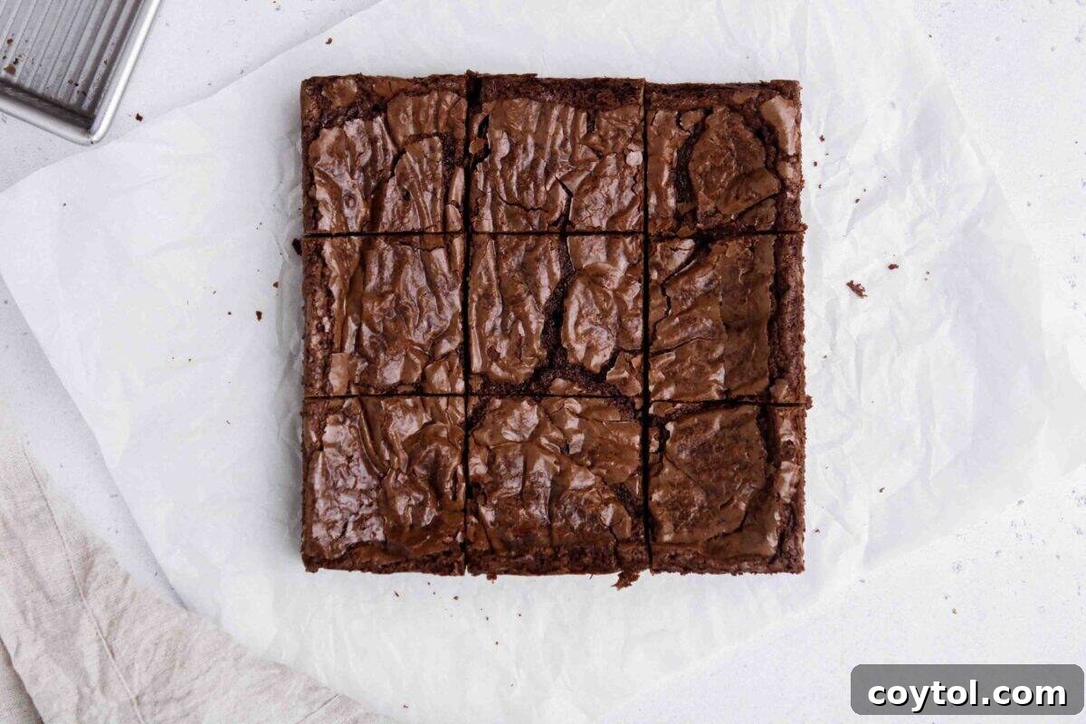 Overhead shot of upgraded boxed brownies, neatly sliced into nine squares on parchment paper, displaying shiny crinkly tops and a deliciously fudgy texture, thanks to 10 secret hacks.