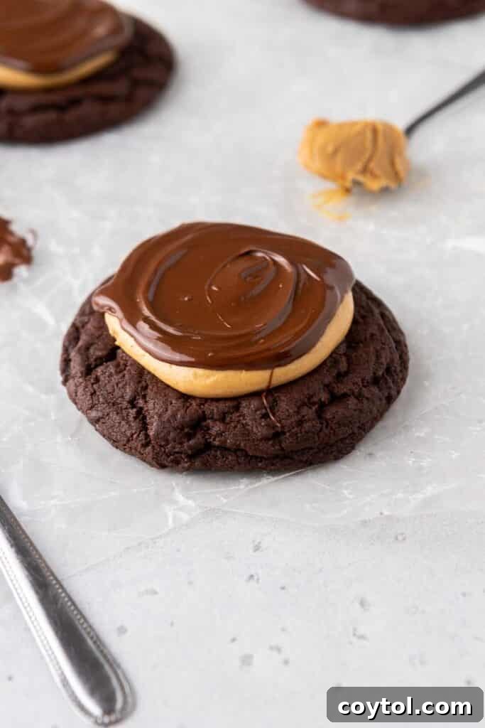 A delightful Crumbl peanut butter brownie cookie on parchment paper, showcasing a thick chocolate brownie cookie base lavishly topped with creamy peanut butter and a glossy chocolate ganache drizzle, inspired by Crumbl and buckeye candy.