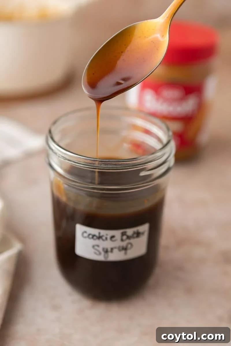 A spoon drizzling homemade cookie butter syrup into a labeled mason jar showing the thick, pourable consistency.