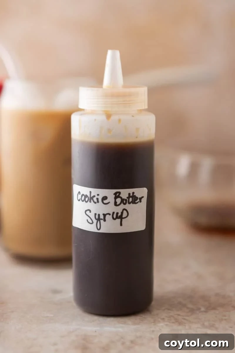 Homemade cookie butter coffee syrup in a squeeze bottle with a cookie butter iced latte in the background.