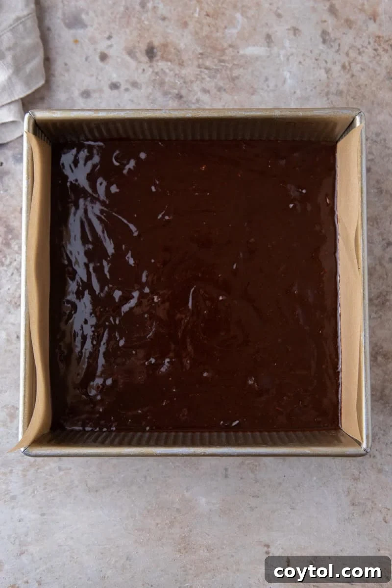 Espresso brownie batter poured into a parchment lined 8x8 metal baking pan
