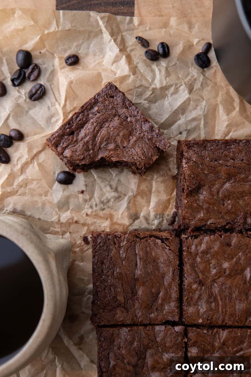 Overhead shot of sliced brownies on parchment with scattered coffee beans and a ceramic mug of espresso