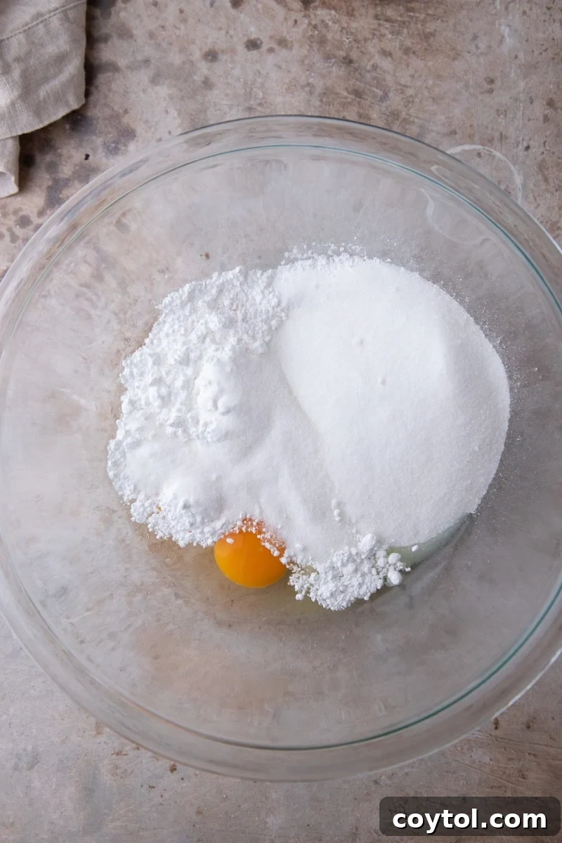 Eggs, granulated sugar, and powdered sugar in a glass mixing bowl before whipping