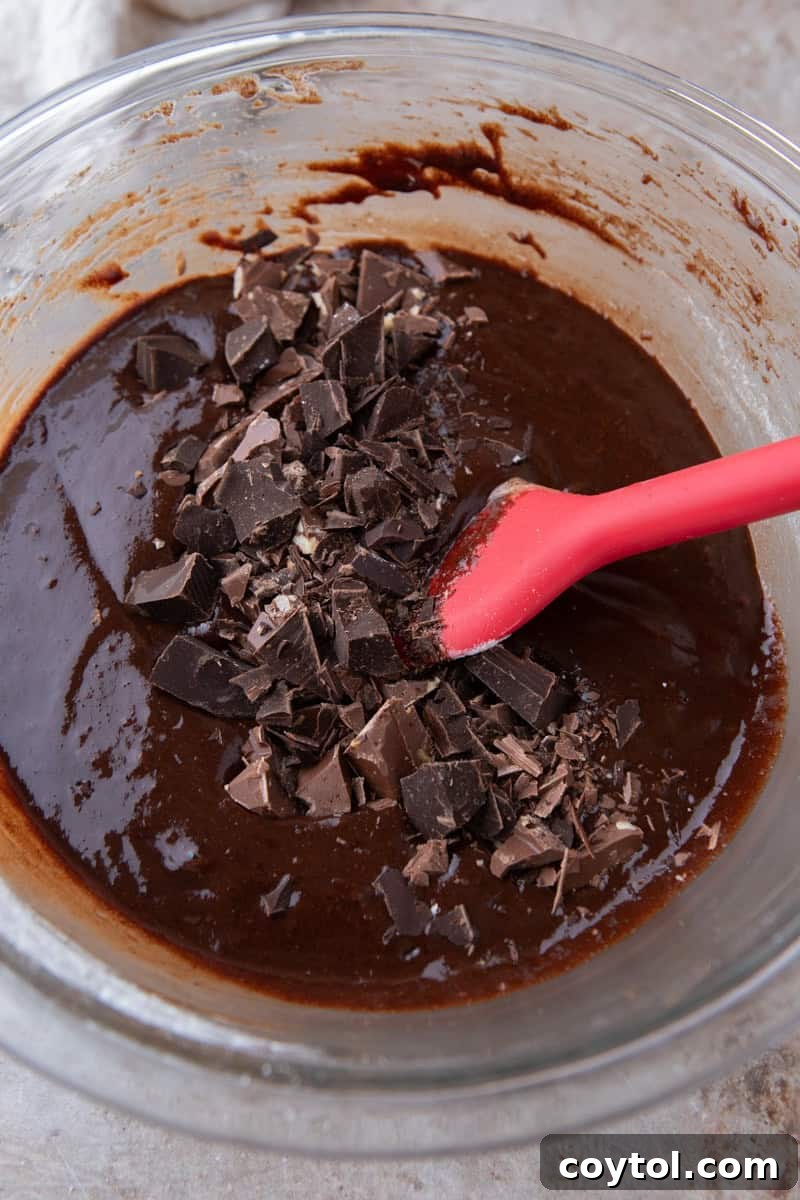 Folding chopped dark chocolate chunks into brownie batter with a red silicone spatula
