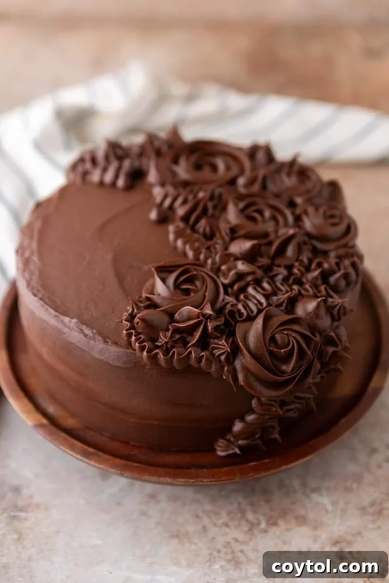 A beautifully finished layered marble cake, generously frosted with chocolate cream cheese frosting and elegantly decorated with piped rosettes, presented on a rustic wooden plate