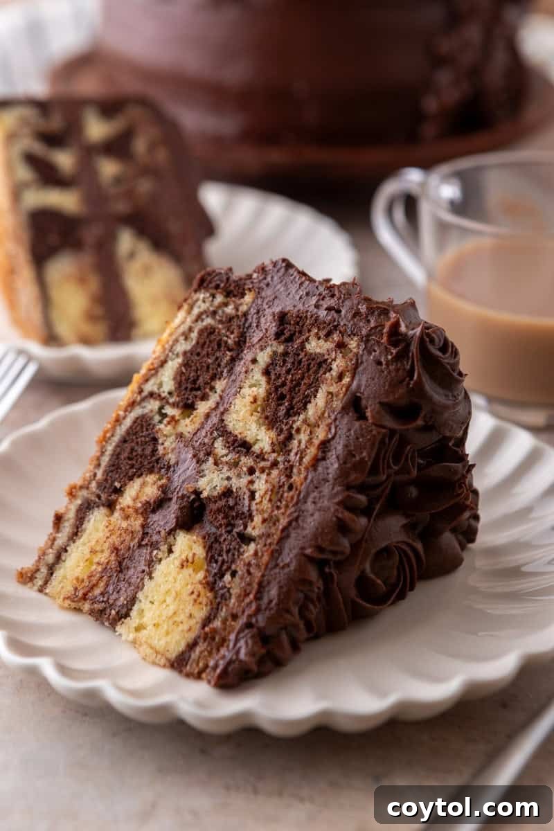A beautiful slice of marble cake with chocolate frosting on a white scalloped plate, with a cup of coffee in the soft-focus background, highlighting the cake's appeal