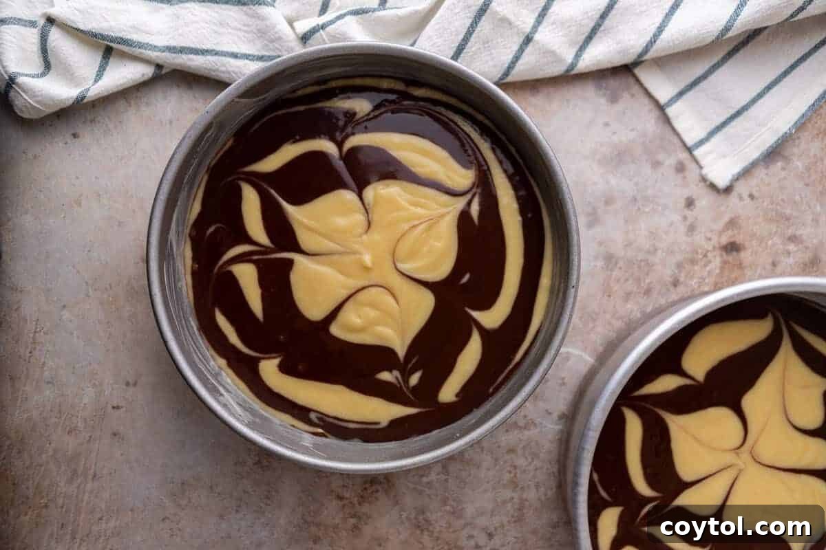 Vanilla and chocolate cake batter beautifully swirled together in two round cake pans, ready to be baked to perfection