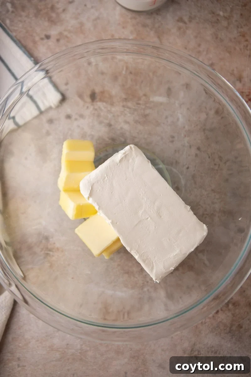 Block of cream cheese and cubes of softened butter in a glass mixing bowl