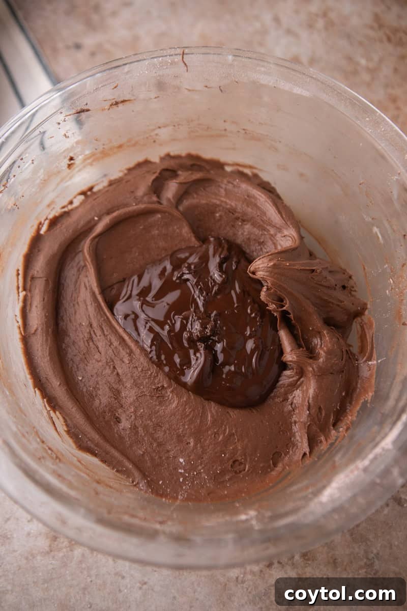 Melted dark chocolate added to the frosting in a glass bowl