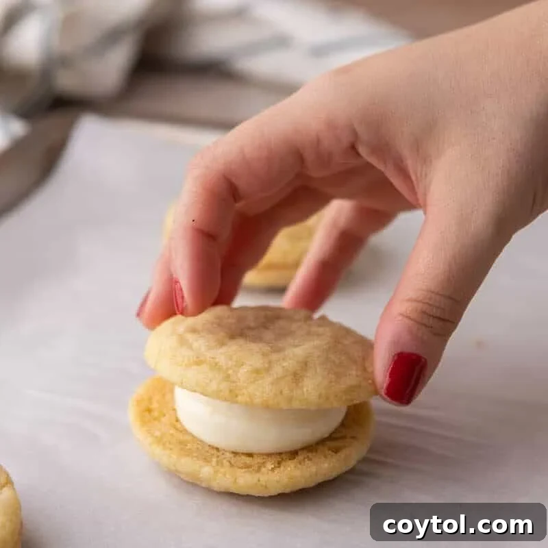 A hand placing the top cookie onto a cream cheese frosted lemon sandwich cookie to assemble it.