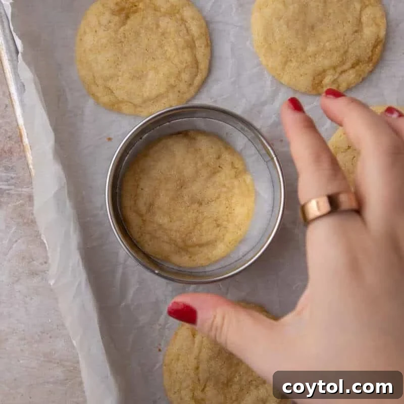 Round cookie cutter being used to swish a freshly baked lemon cookie back into a perfect circle.