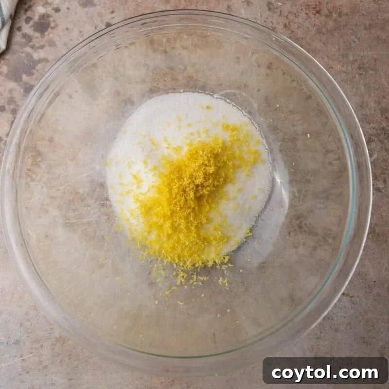 Glass bowl with granulated sugar and fresh lemon zest before being rubbed together to release oils.