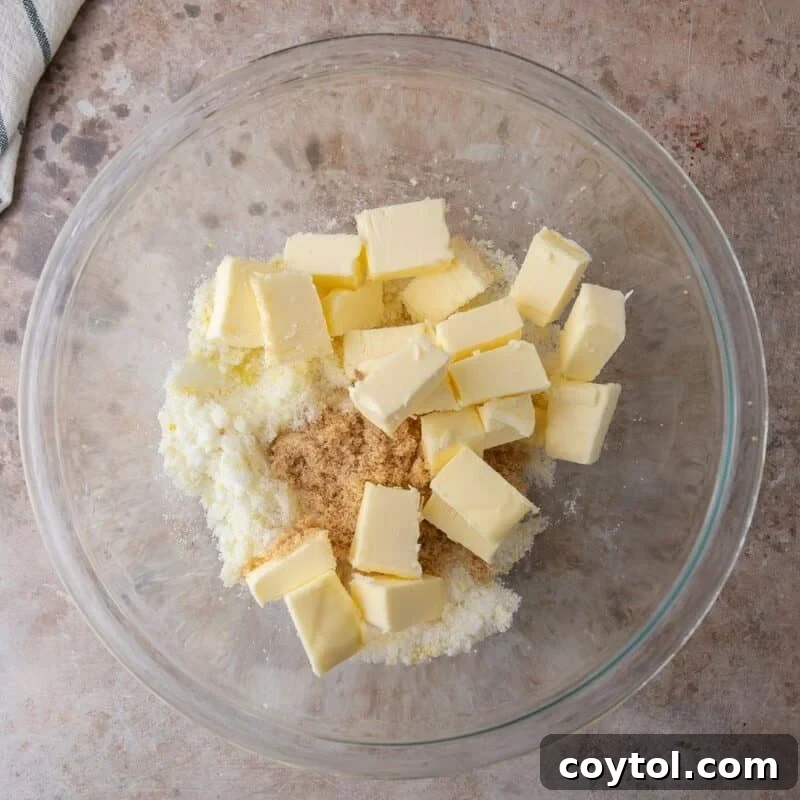 Cubed Plugrà butter added to lemon sugar in a glass bowl, ready to be creamed for cookie dough.