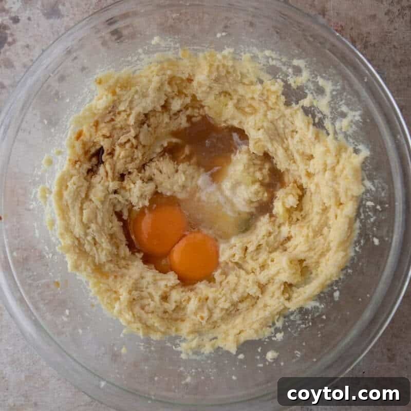 Eggs and lemon juice added to creamed butter and sugar in a glass bowl for lemon cookie dough.