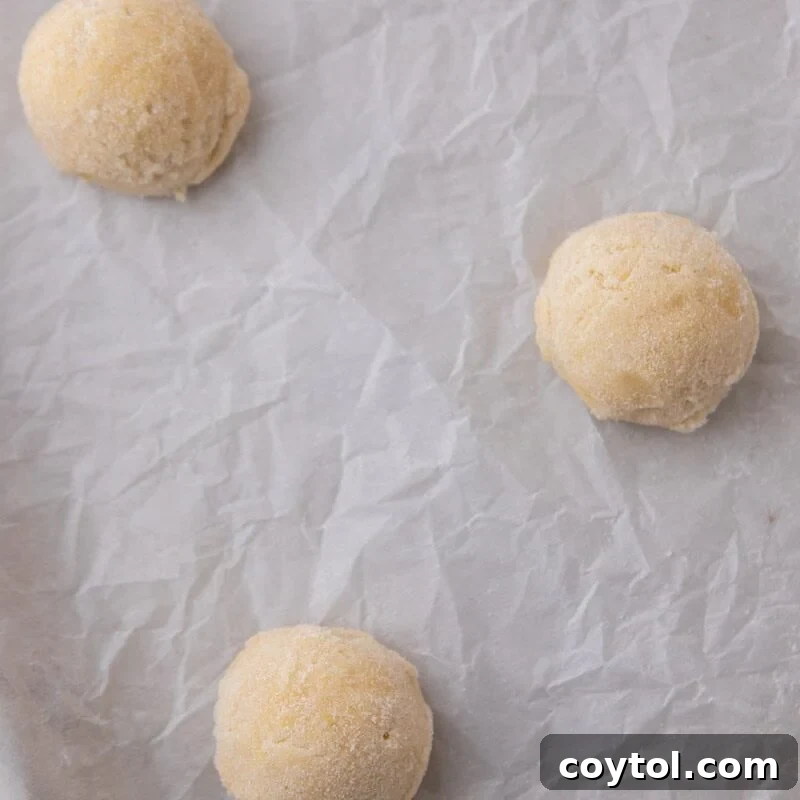 Three scooped lemon cookie dough balls rolled in sugar on a parchment-lined baking sheet.