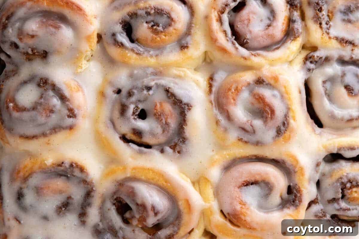 A baking pan filled with freshly baked mini cinnamon rolls, drizzled with a light cream cheese glaze, showing the intricate cinnamon swirls.