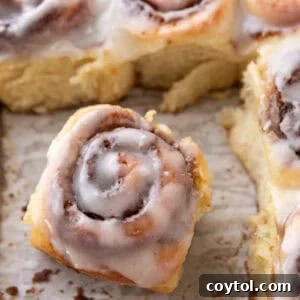 A single perfect mini cinnamon roll pulled from the pan, showing its soft texture and cream cheese glaze.