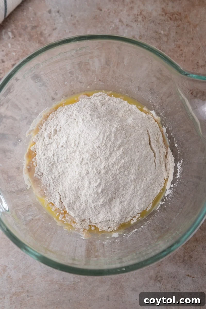 All-purpose and bread flour are added on top of the wet ingredients in the glass mixing bowl before mixing.