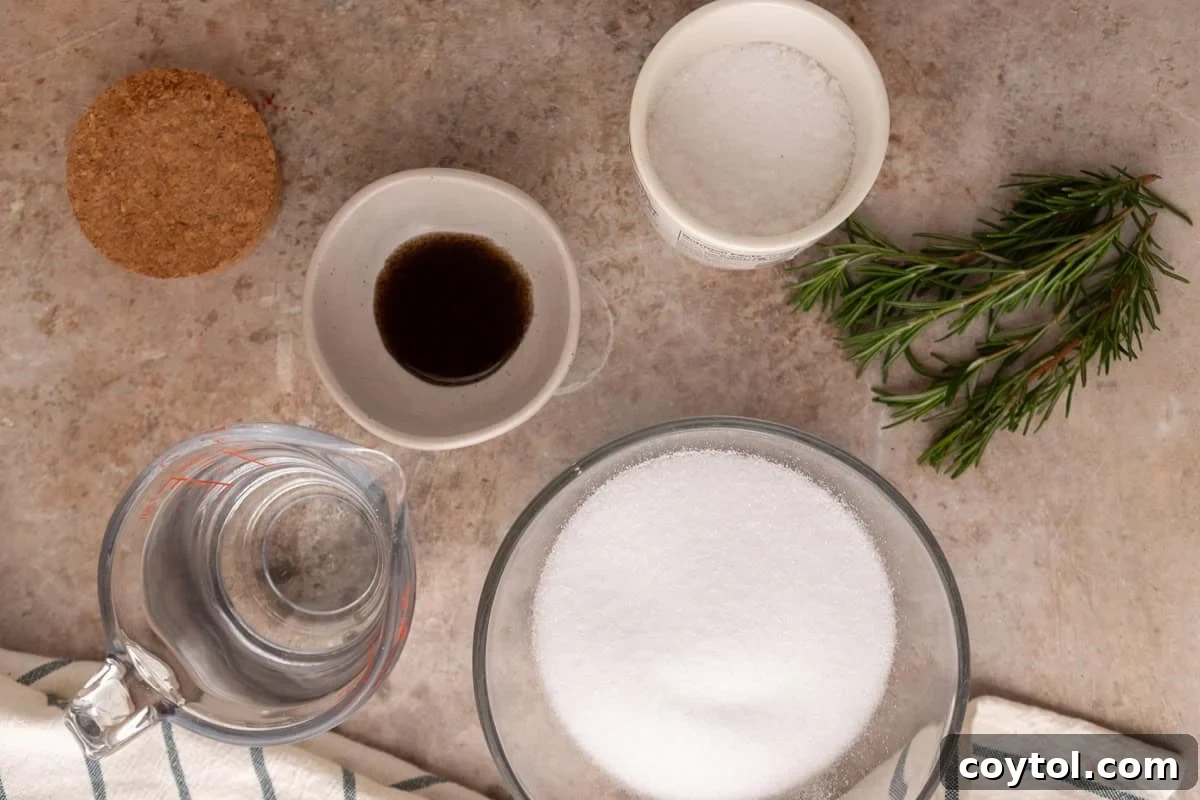 An array of ingredients for rosemary vanilla syrup laid out on a surface, including a bowl of sugar, a pitcher of water, fresh rosemary sprigs, a jar of vanilla bean paste, and a small bowl of sea salt.