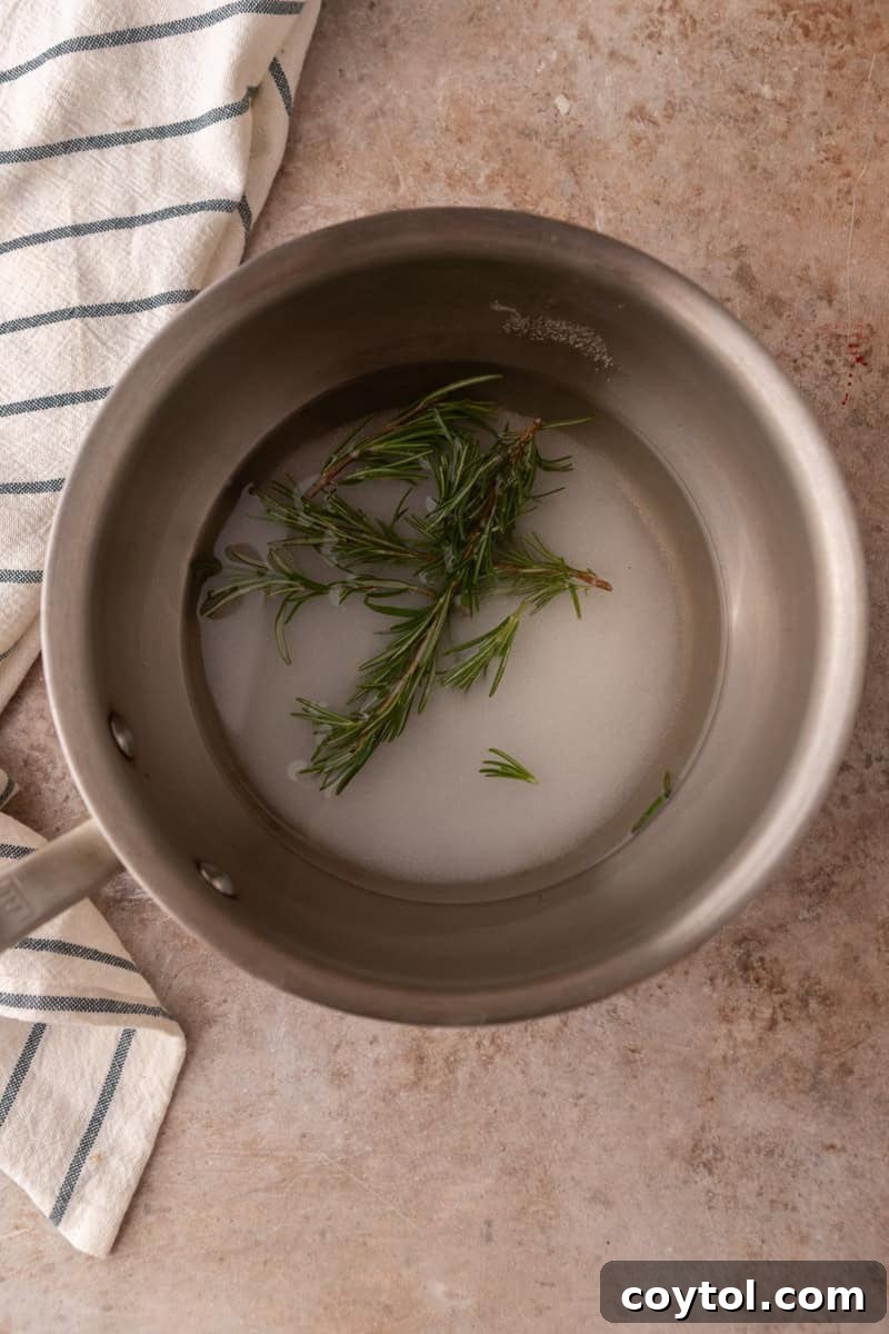 Fresh rosemary sprigs, sugar, and water in a saucepan, ready to be simmered for the simple syrup.