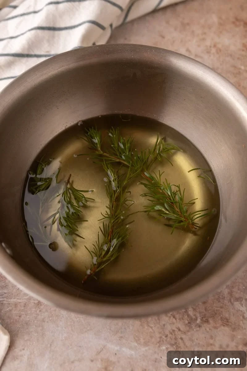 The finished rosemary simple syrup in a saucepan, with the steeped rosemary sprigs still inside.