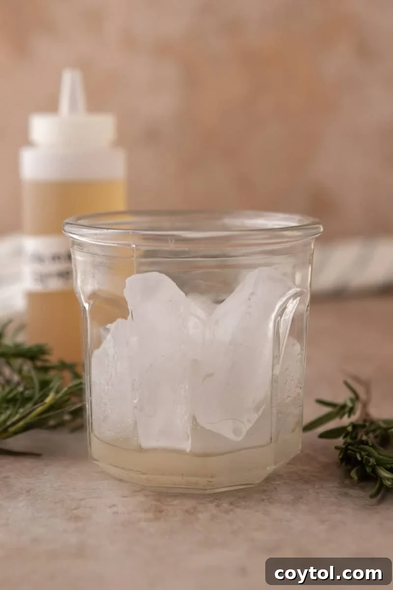 A tall glass filled with ice, with a layer of homemade rosemary vanilla syrup at the bottom, ready for milk and espresso.