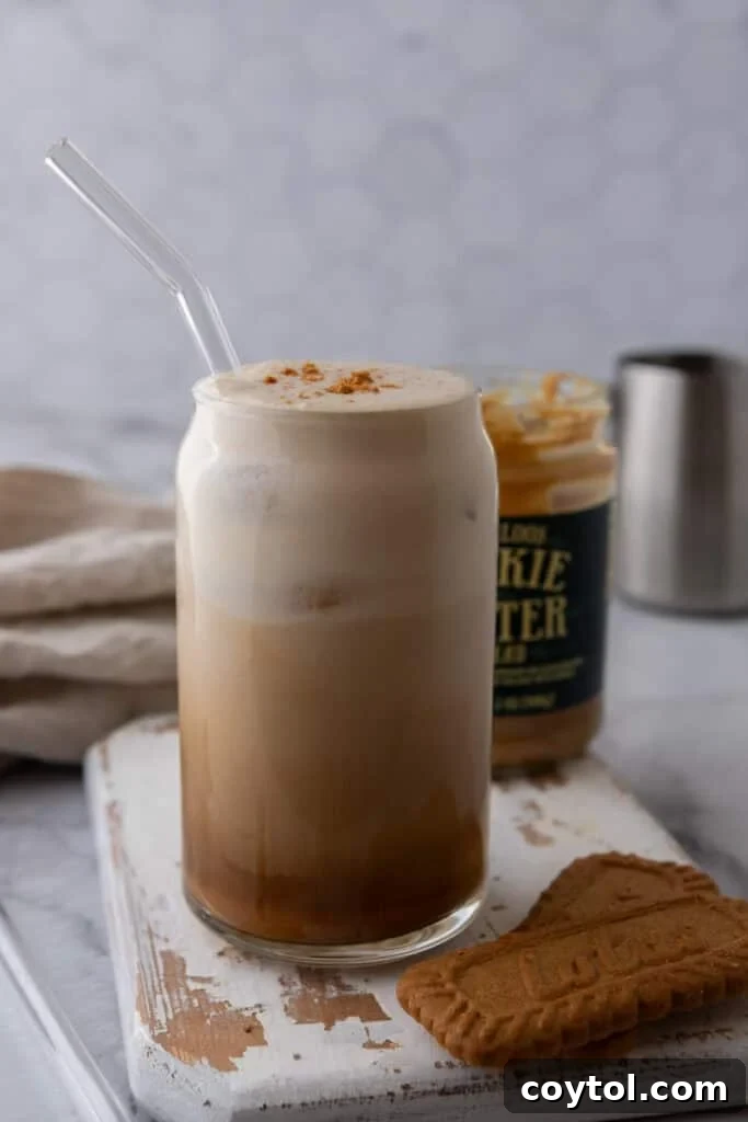 A refreshing iced cookie butter latte in a glass, with Biscoff cookies on the side and a layer of cold foam, a perfect Starbucks copycat for Mother's Day.
