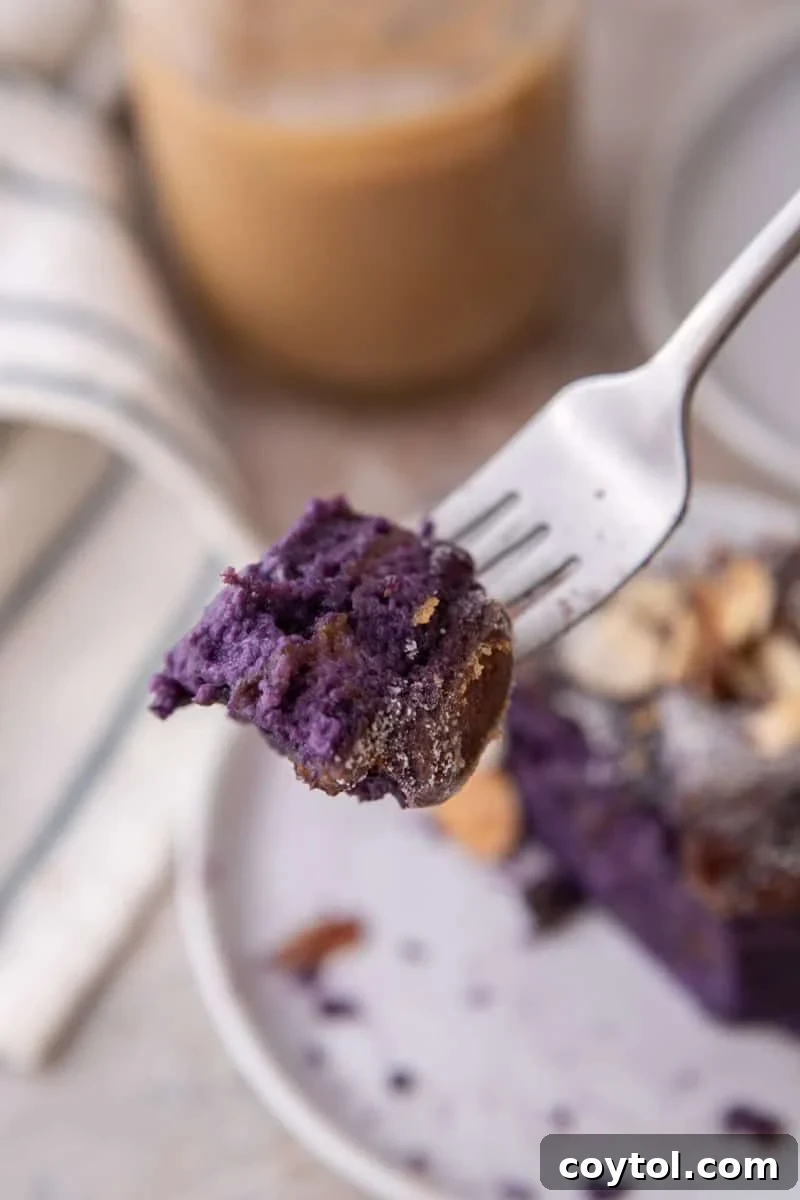 A close-up view of a fork holding a bite-sized piece of the soft purple ube French toast, with a coffee cup blurred in the background.